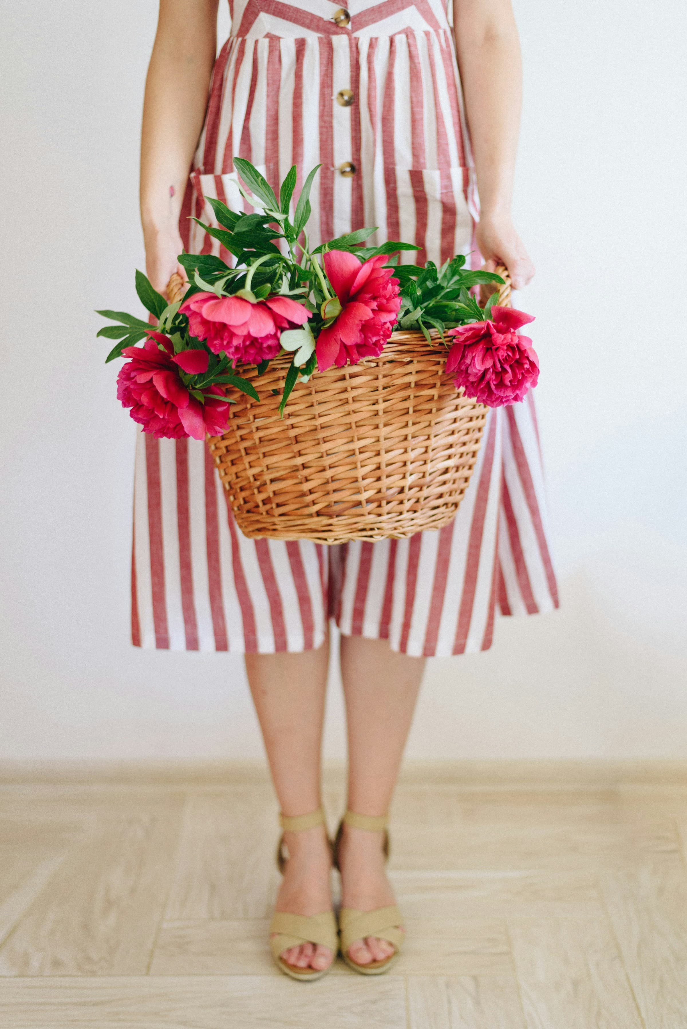 A woman holding a basket of pale peonies in soft afternoon light